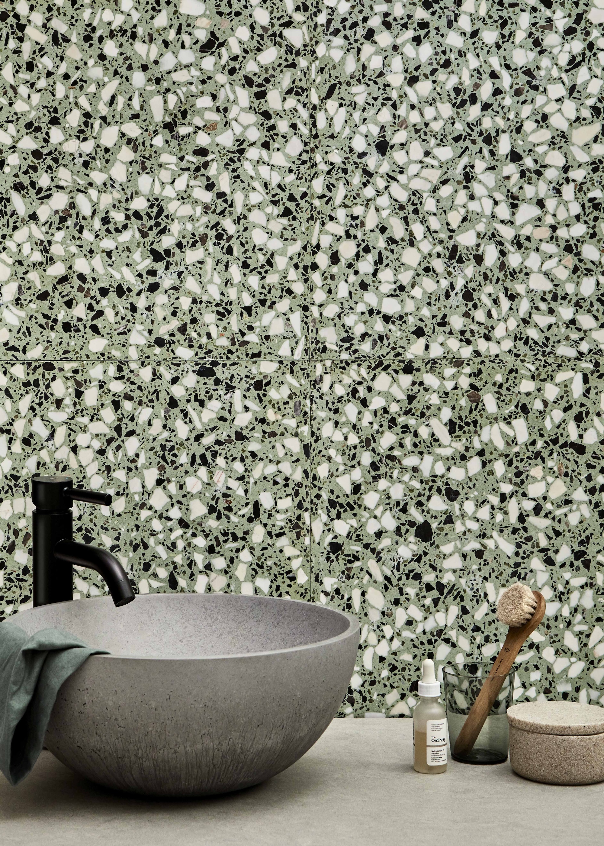 Colorful green bathroom tiling with a grey sink and black hardware