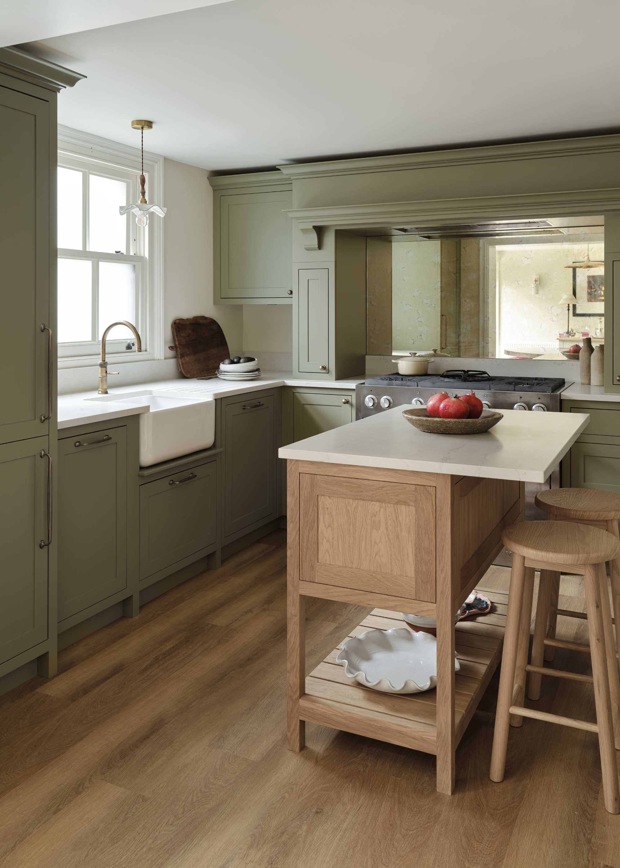 A sage green traditional kitchen with a small wooden island with bar stool on one side and a mirrored backsplash above the cooker