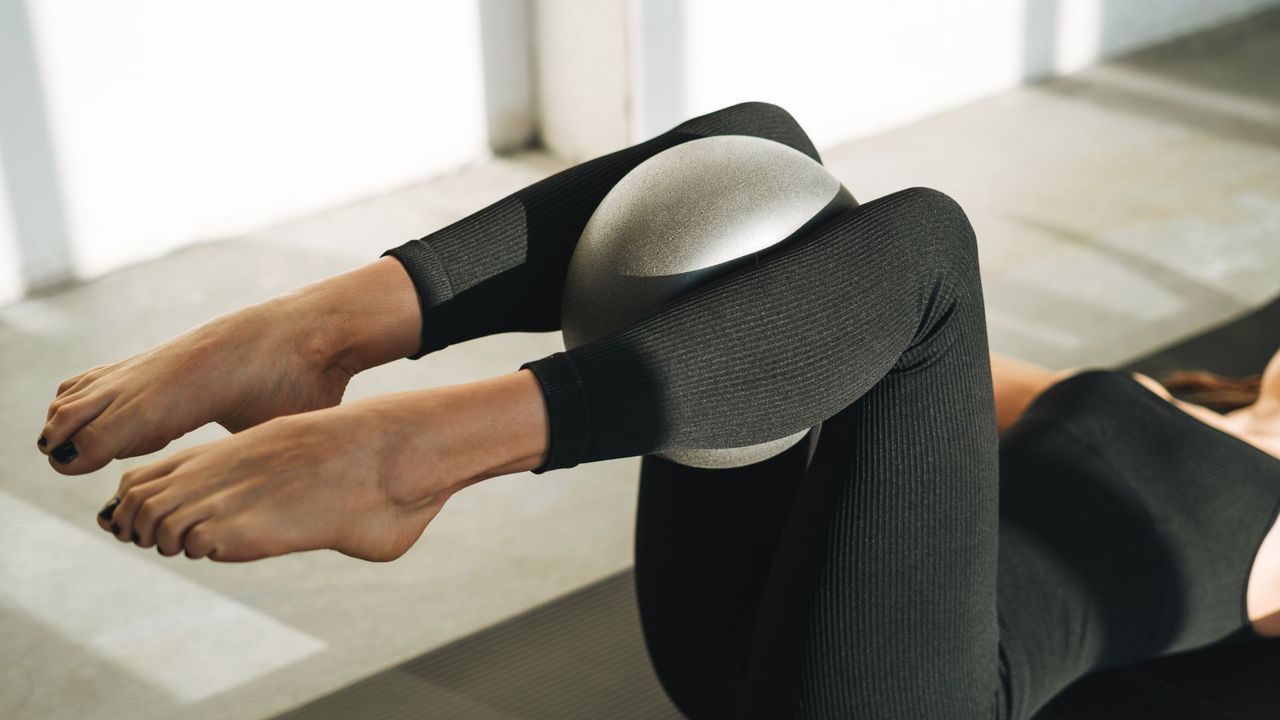 Woman holding Pilates ball between knees lying on yoga mat doing 15-minute Pilates workout at home