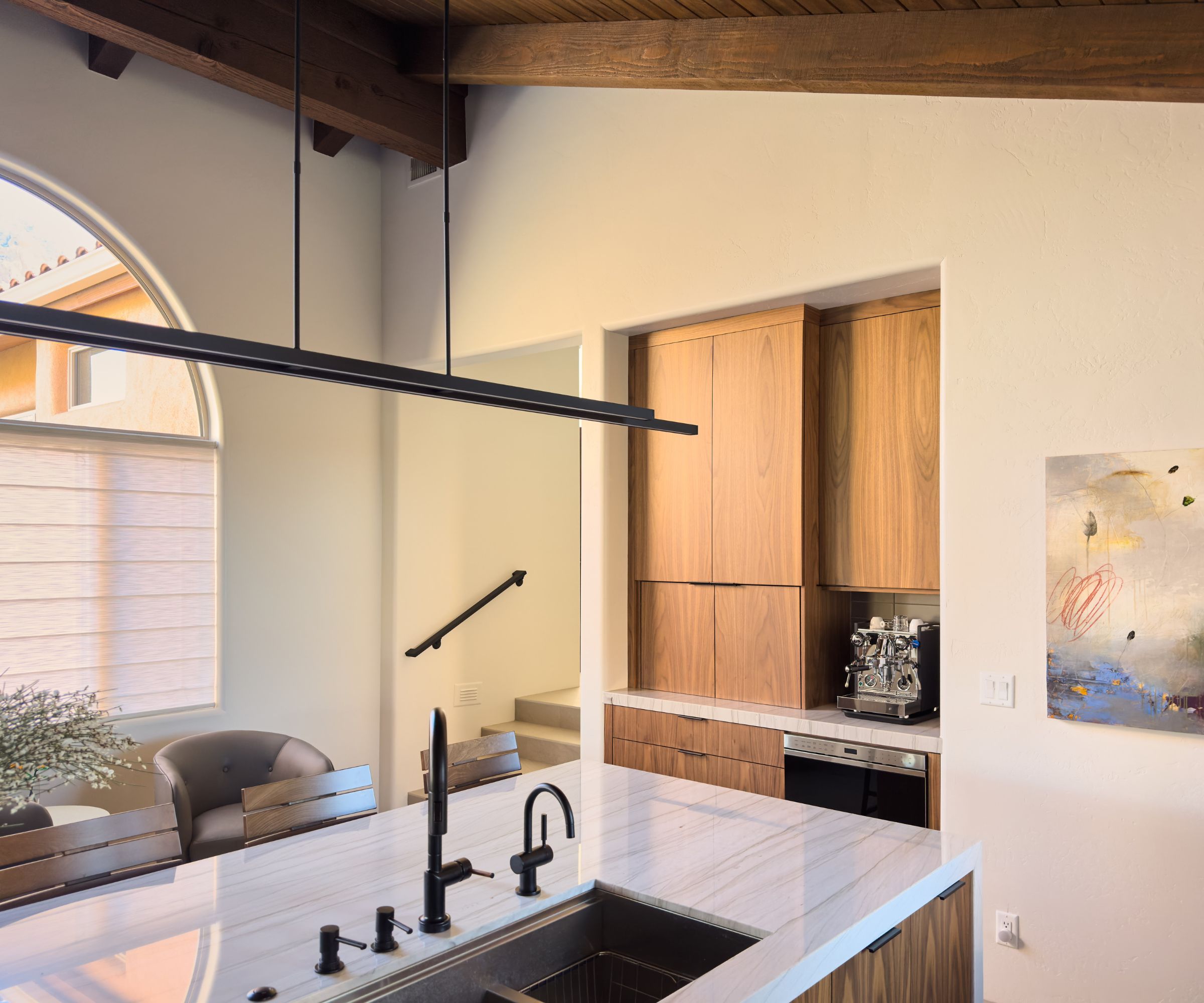 Close up of coffee station in kitchen and side of kitcen island. Artwork on wall, large pendant light above island.
