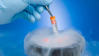 a gloved hand uses tweezers to hold a test tube over dry ice.