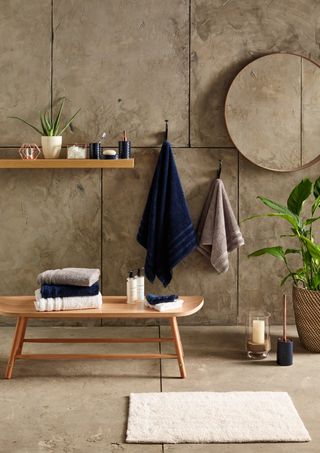 Neutral stone bathroom with deep blue and neutral bath towel, circular mirror and wooden storage