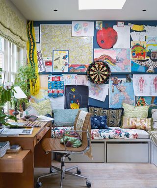 Colorful, maximalist office with walls decorated with art, wooden desk and desk chair facing window, collection of books and ornaments