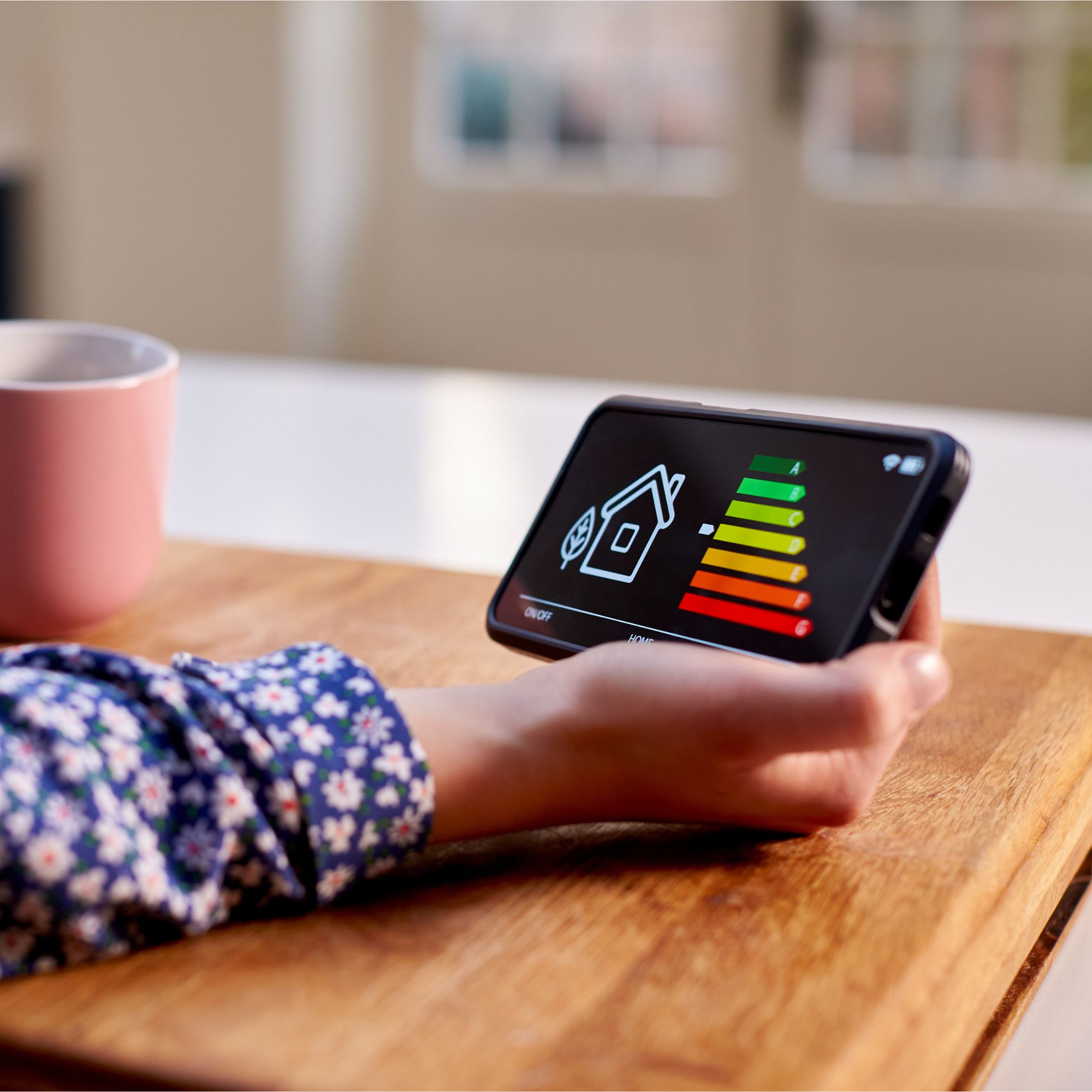 Hand holding a smart energy meter, with a pink coffee cup to the side