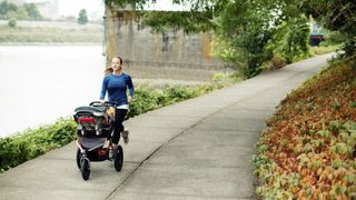 Woman jogging with baby stroller on footpath by river