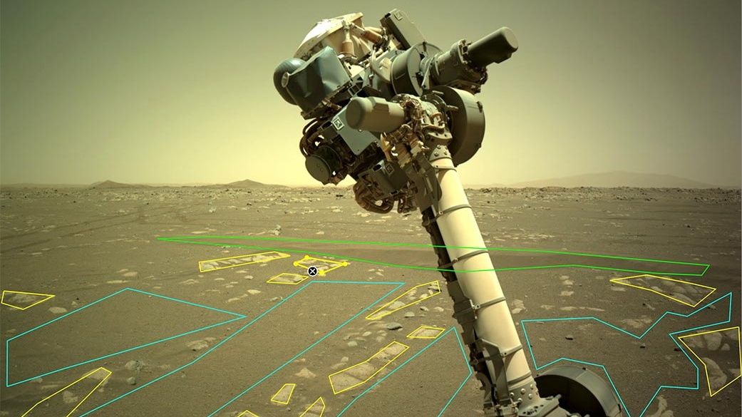 A robotic arm is seen in the foreground. In the background is the barren land of Mars with manually drawn lines to denote different areas.