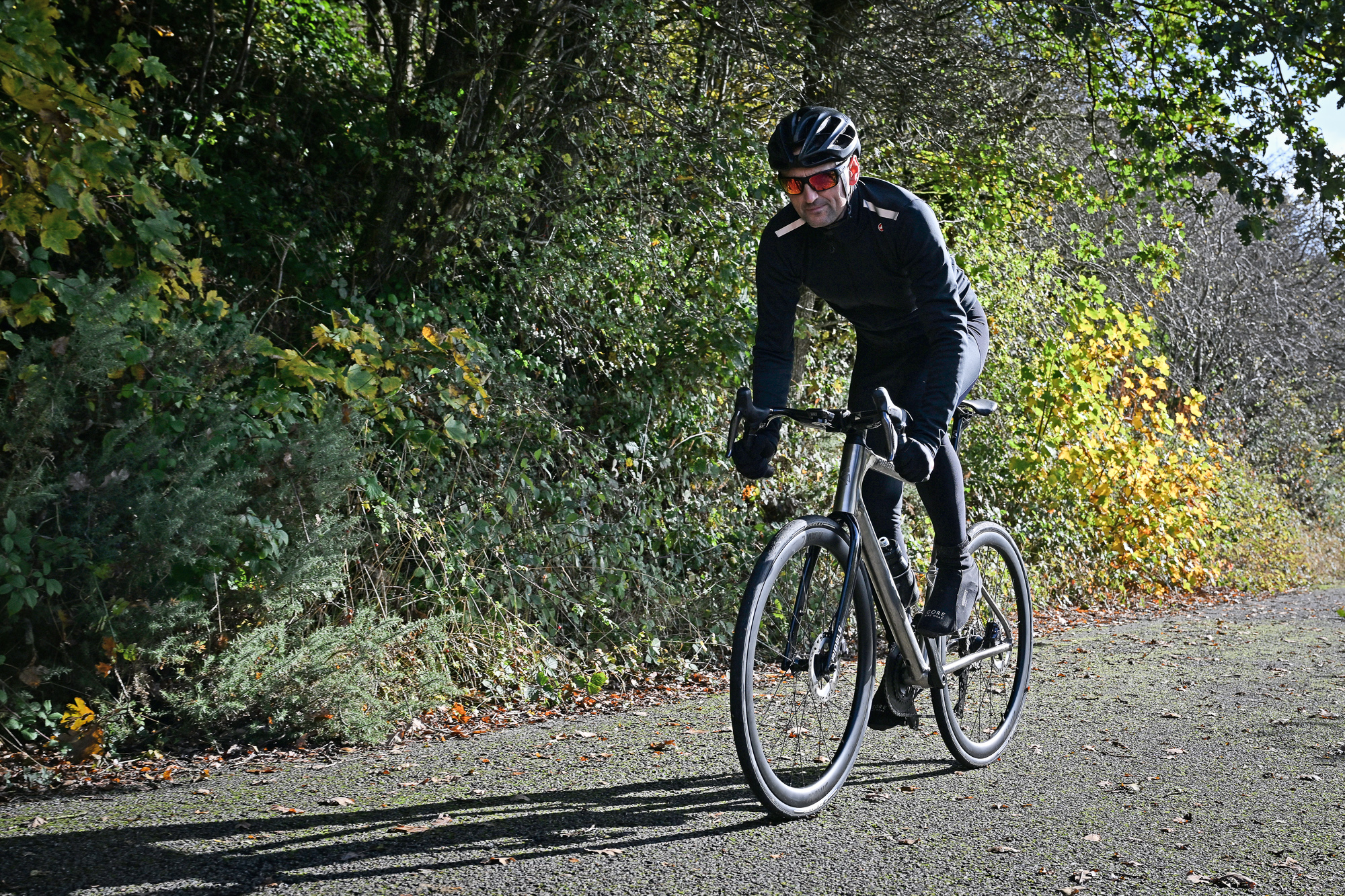 man riding a titanium bike on a leafy country lane