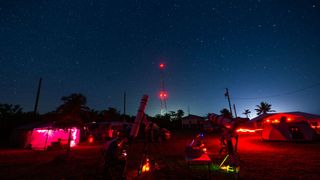 red lights from headtorches and torches are the only artificial light visible under a starry sky.