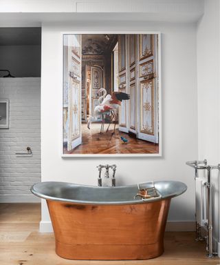 A white bathroom with a copper bath below a large artwork and a metro tiled wall