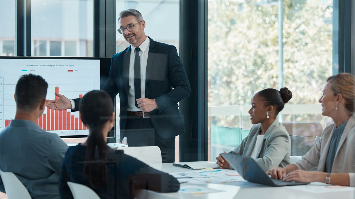 CEO standing in an open plan office space speaking to team during a boardroom meeting.