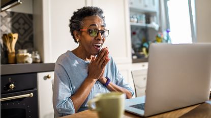 An older woman gazes at her laptop with a look of joy on her face.