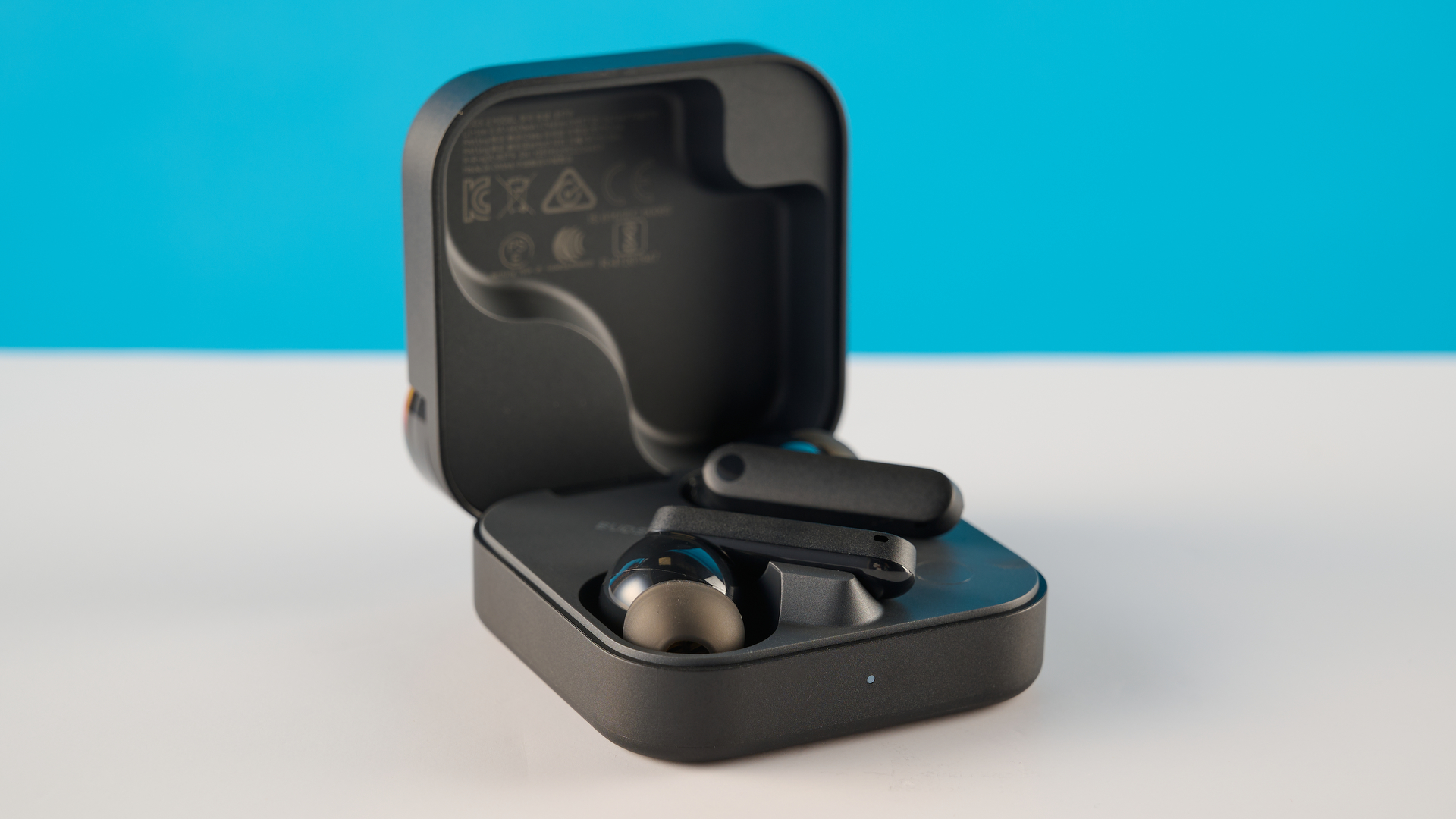 CMF Buds 2 in Dark Gray photographones on a gray table in front of a blue background