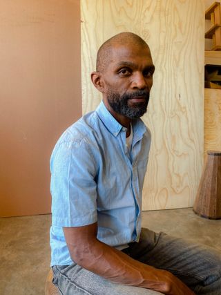 Designer and maker Peter Mabeo wearing a blue short sleeve shirt and jeans in his workshop in Botswana