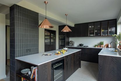 Black kitchen with kitchen island storage a tiled wall and copper pendants overhead