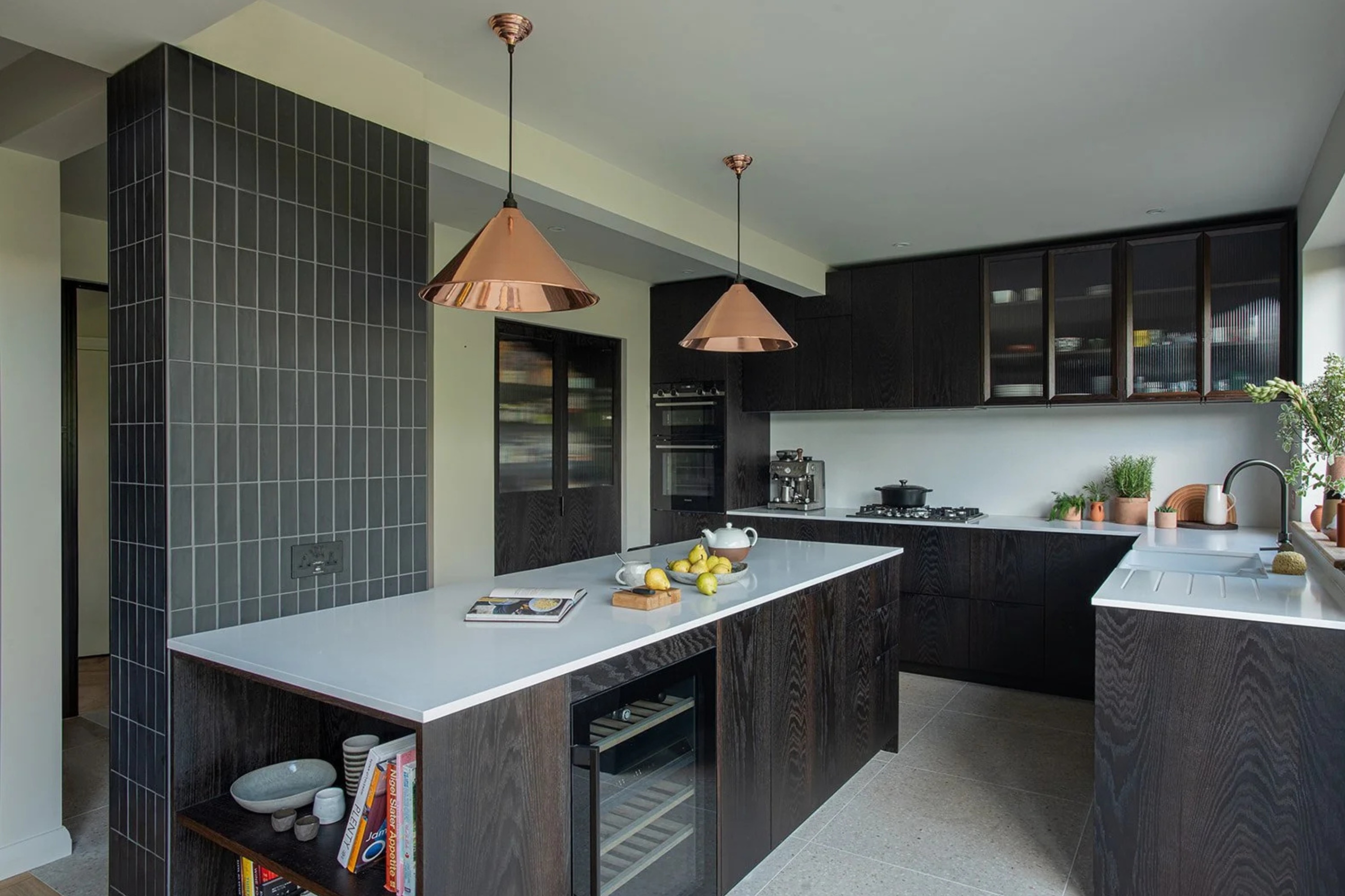 Black kitchen with kitchen island storage a tiled wall and copper pendants overhead