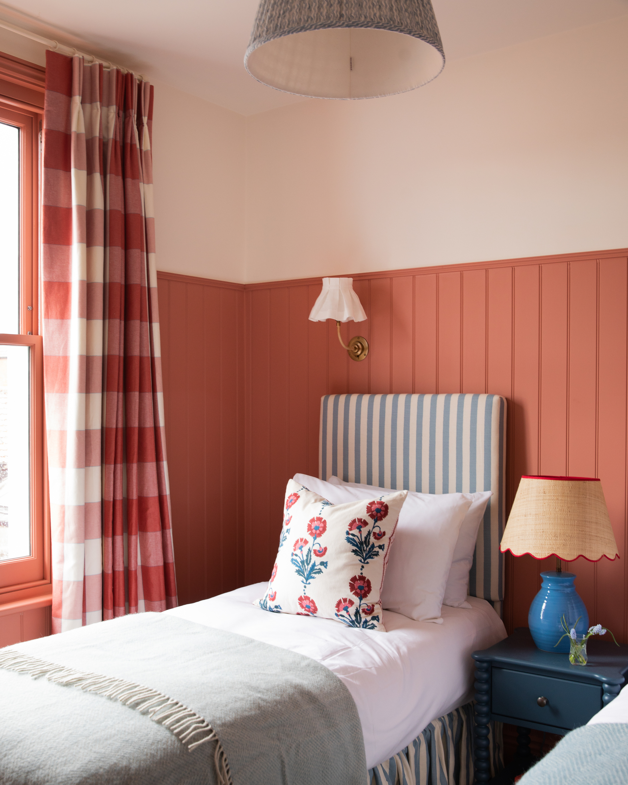 Image of a twin bedroom with salmon pink wood paneling that goes three-quarters of the way up the wall, then the top and ceiling are a pink-toned white.