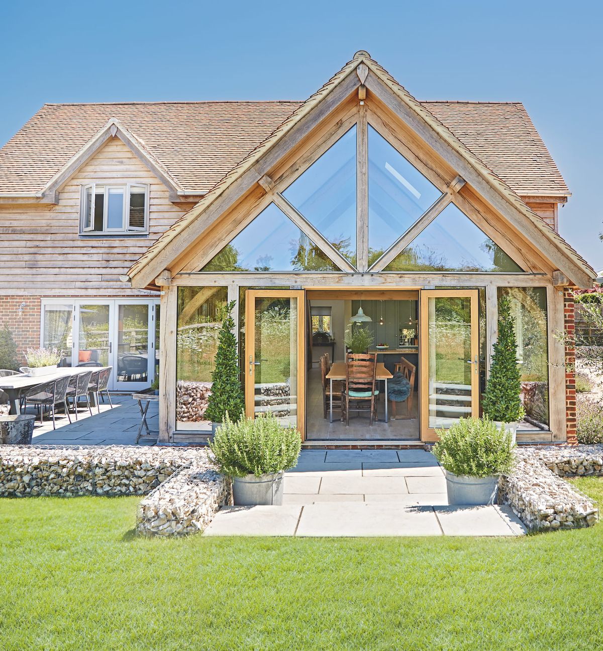 An oak framed house with a large glass and timber extension leading out onto a small patio and a green lawn