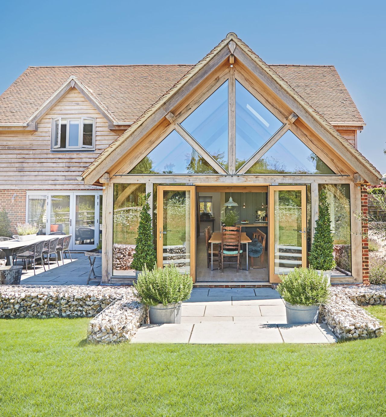 An oak framed house with a large glass and timber extension leading out onto a small patio and a green lawn