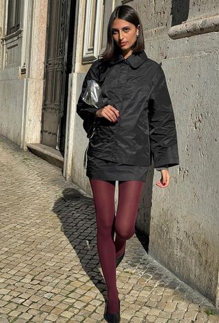 winter tight outfit shown in a photo of a woman wearing a black jacket with a matching mini skirt styled with red tights, black heels, and a silver clutch bag