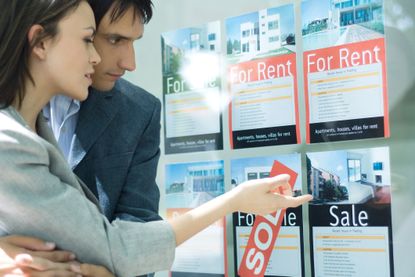 Couple looking at posted listings about homes for sale and rent, pointing to a listing