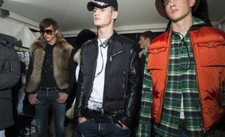 Three male models wearing looks from Dsquared2's collection. One model is wearing sunglasses, a dark top, jeans and fur gilet. Another model is wearing a black and white cap, white top, jeans and a black quilted jacket. And the last model is wearing a hat, green plaid shirt and orange gilet