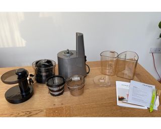 Various parts of Hurom H-AA slow juicer with instruction manual on wooden dining table
