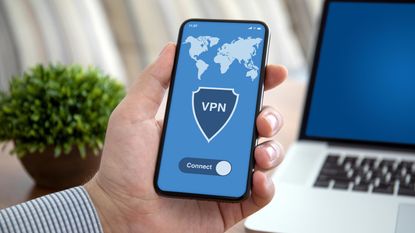 male hand holding phone with app vpn over laptop