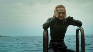 A still from the movie The Dive in which one of the characters is looking distraught and wearing a wetsuit while climbing out of the sea.