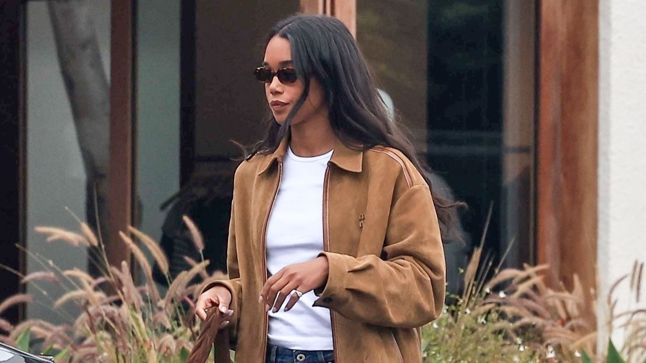 Laura Harrier smartens up dark wash baggy jeans with black leather loafers, a suede zip-up jacket and crisp white tee.
