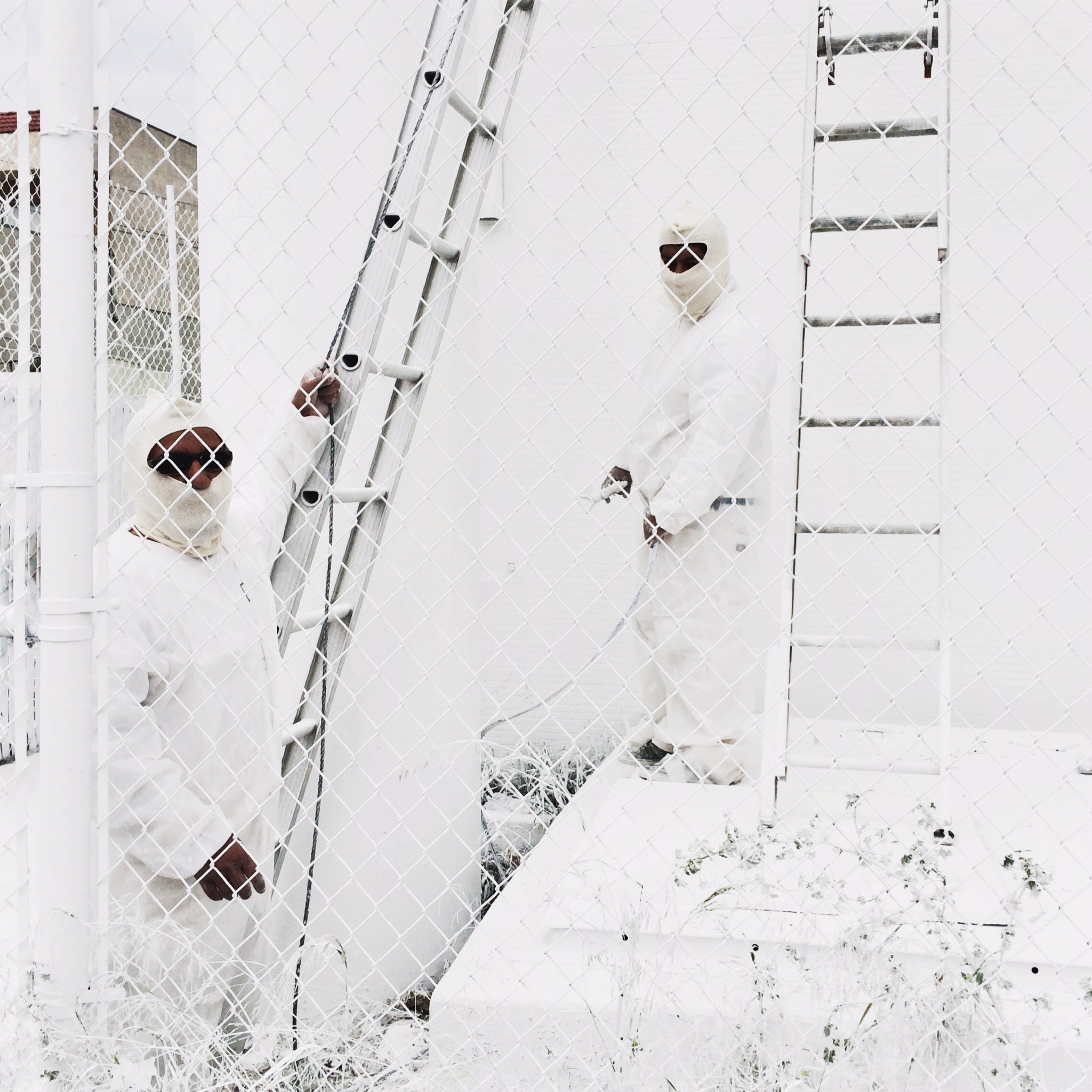 Two men in white overalls work on a white building next to white ladders