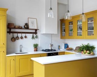 A small kitchen with trio of glass pendants, yellow cabinetry and fruit bowls