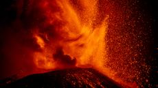 Lava erupts from a volcano in a huge shower of red molten rock.