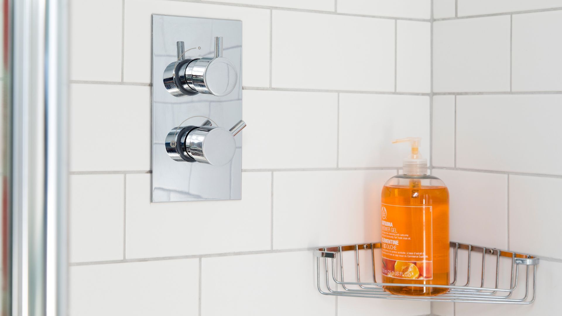 Picture of a tiled show with corner shelf holding body wash, chrome accents and white tile with white grout