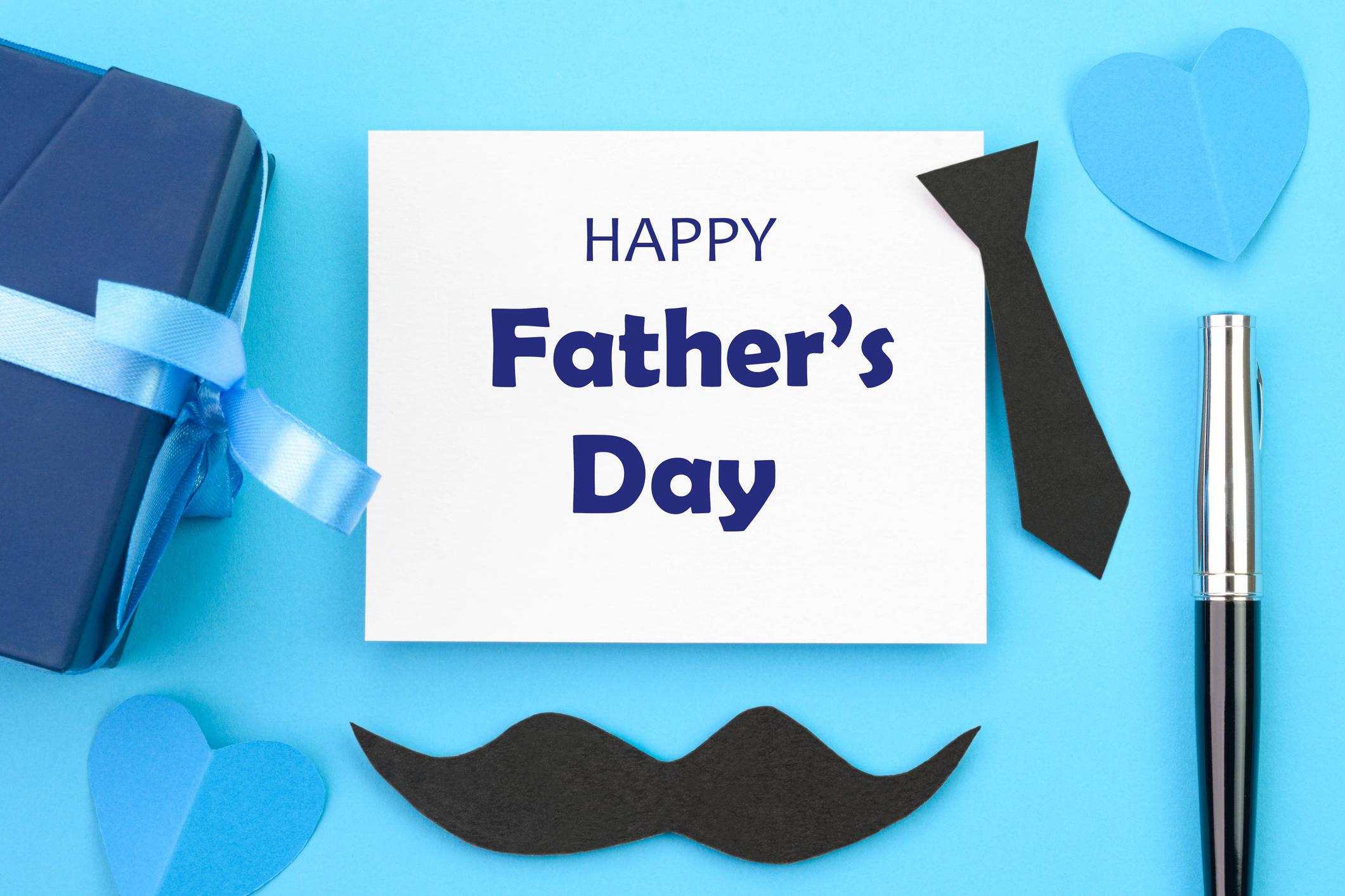  Happy Father's Day card against a blue background. With a black tie and moustache beside the card.  