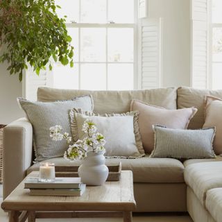 A light-coloured corner sofa with frilled throw cushions on top