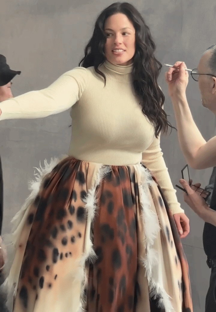 a woman with brown hair in a white shirt and animal print skirt in a moving gif