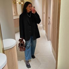 chiara wears black blazer, blue jeans, and tabbis while posing for a mirror selfie