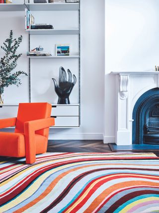 A living room with bright white walls, an orange armchair and multicolored rug