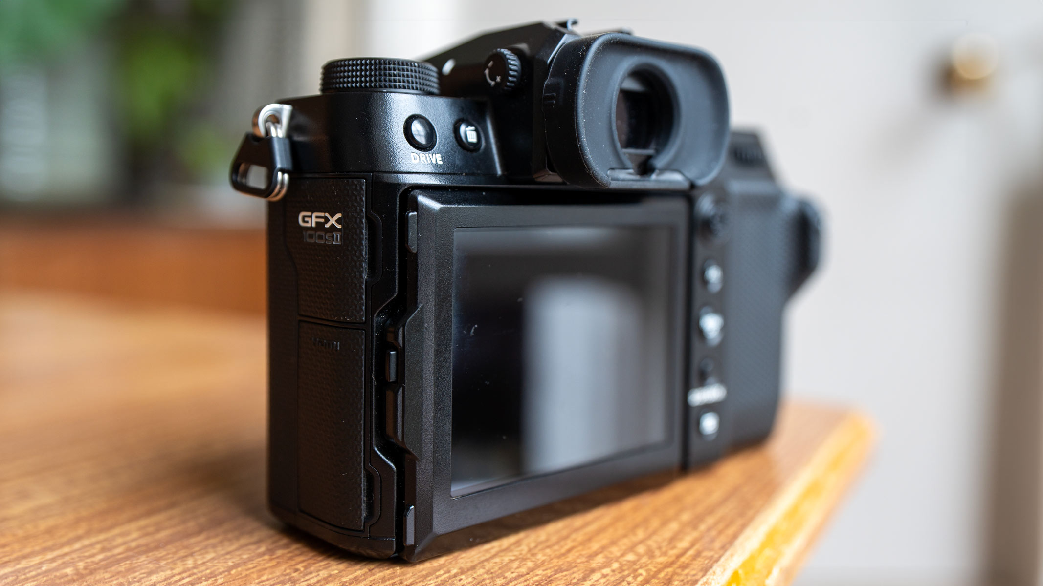 The back of the Fujifilm GFX100S II showing the LCD screen, viewfindern and GFX100S II logo on a wooden table.
