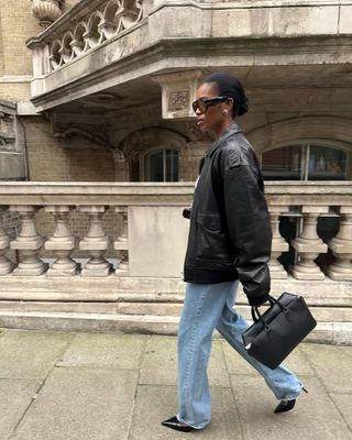 Woman wears leather jacket, blue jeans and black tote bag