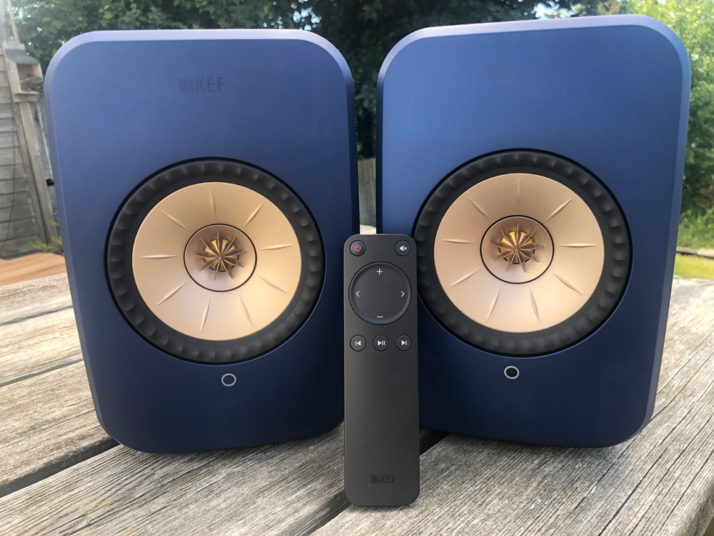KEF LSX II speakers on a wooden table with remote leant up against them