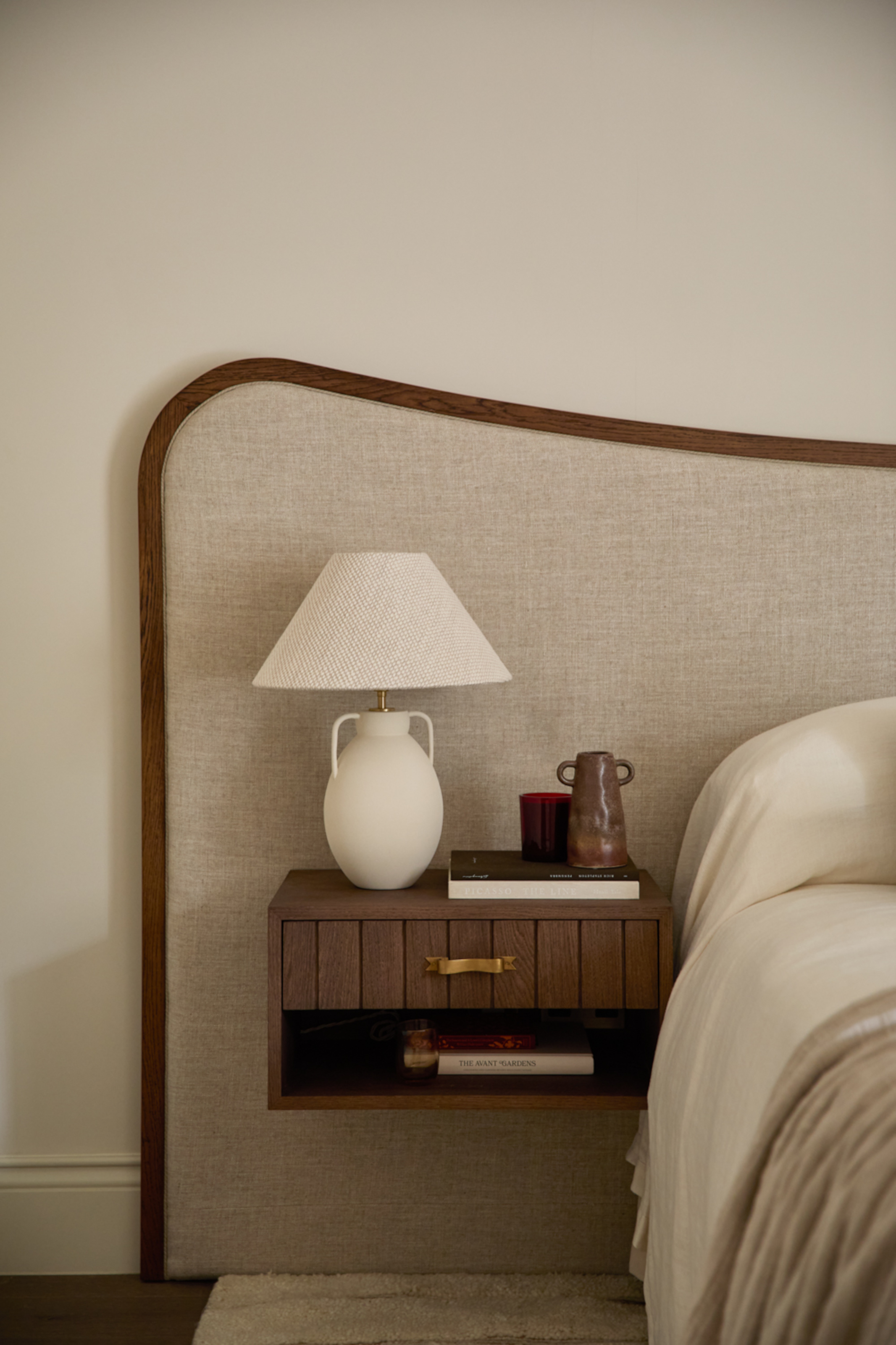 Bed and wooden floating bedside table built into extended wooden headboard with fabric upholstery in beige
