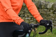 Man sitting on a green bike wearing an orange jacket and black gloves