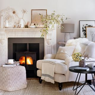 Cosy neutral living room with a comfy armchair next to a fire, and eclectic display on the mantel