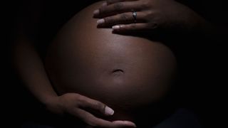 close up on a black woman's pregnant belly with her hands placed on top and bottom