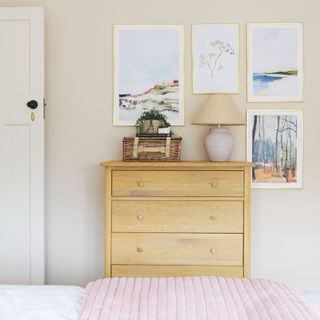 Cream painted bedroom with a wooden chest of drawers topped with accessories, and a gallery wall above it