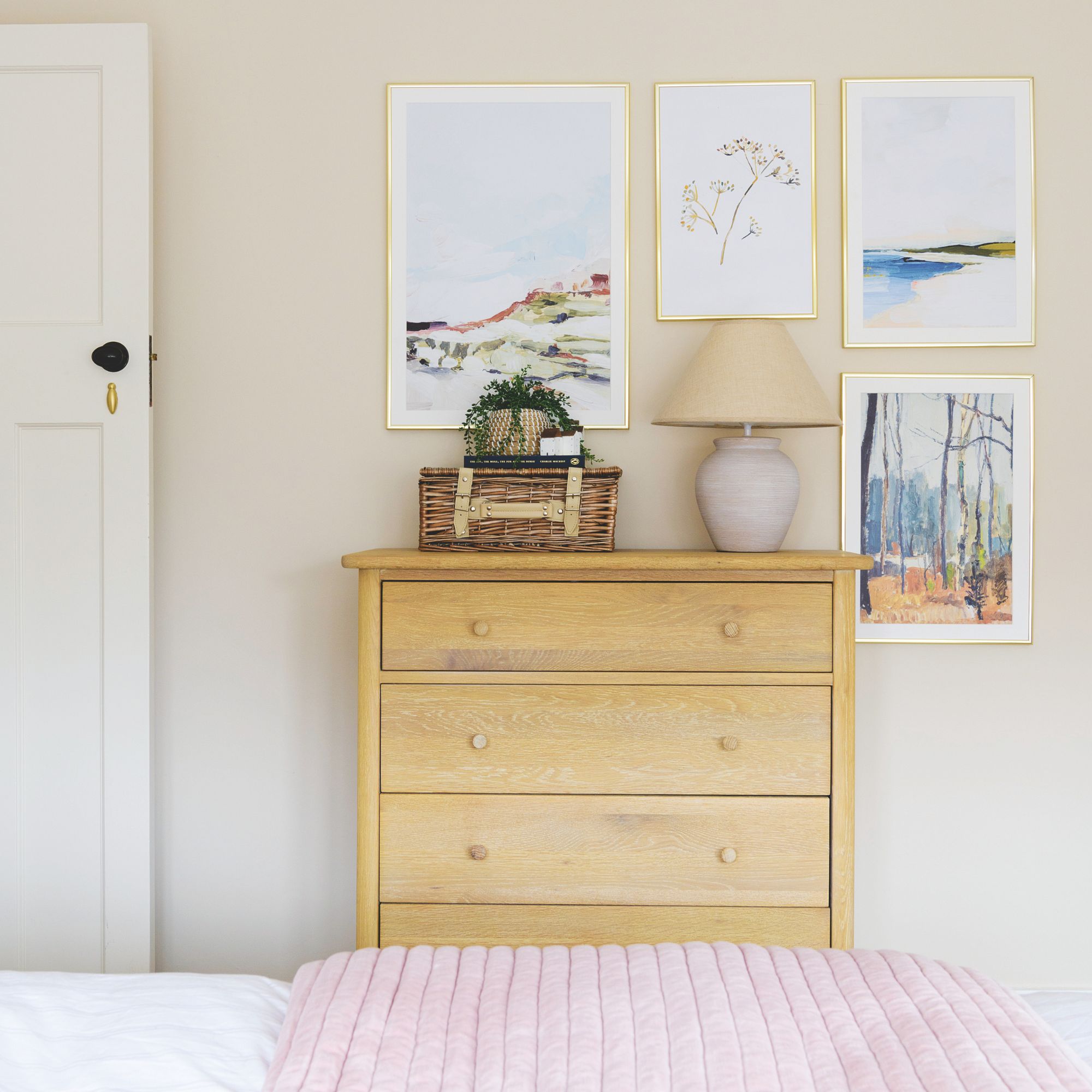 Dormitorio pintado con crema con una cómoda de madera cubierta de accesorios y una pared de la galería sobre él