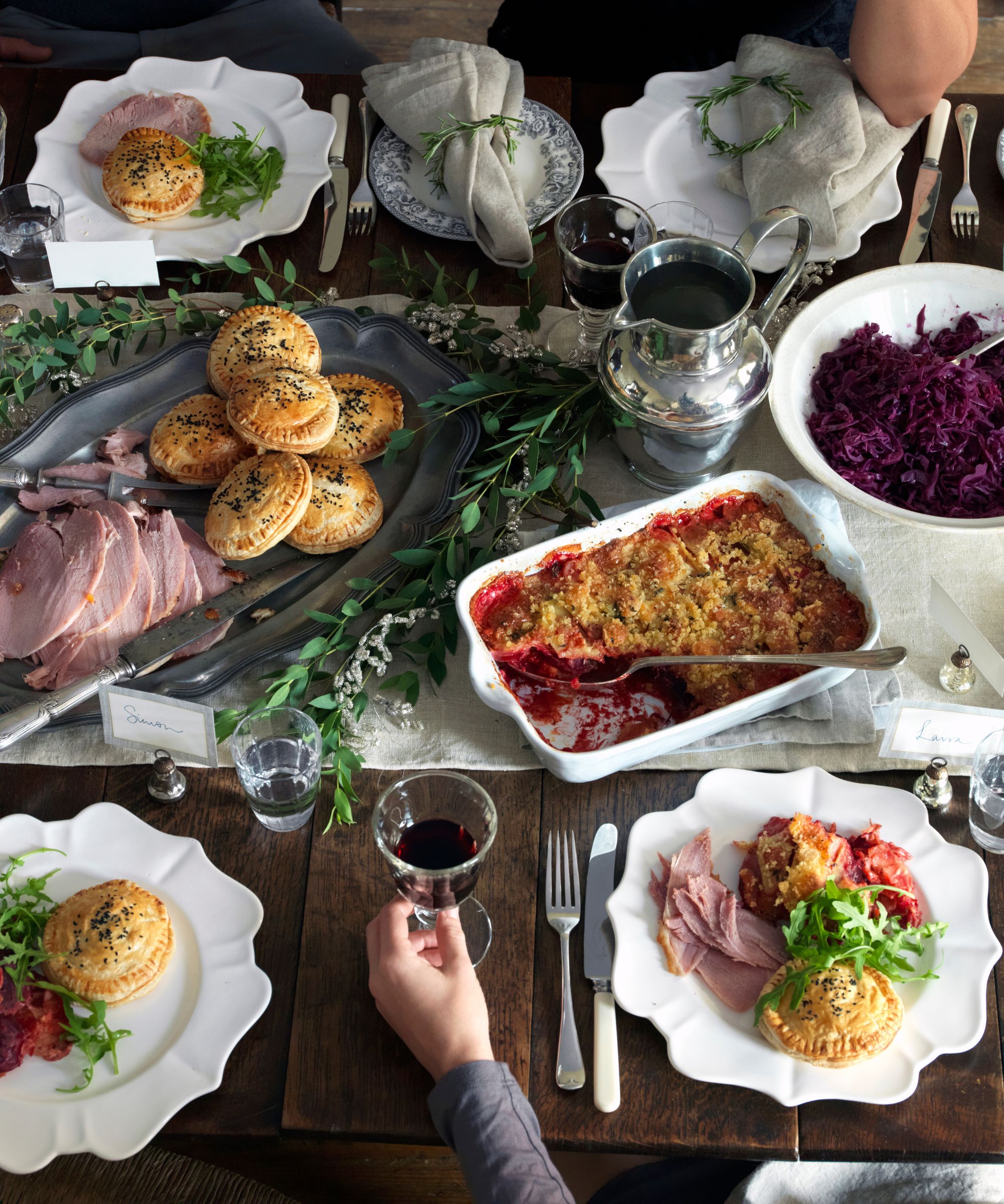 Christmas table set with ham, red cabbage, pies, silverware and greenery