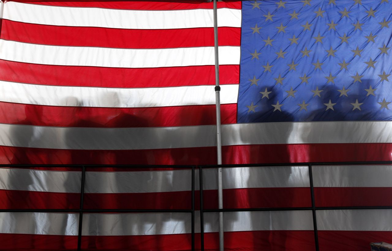 People stand silhouetted against an American flag.