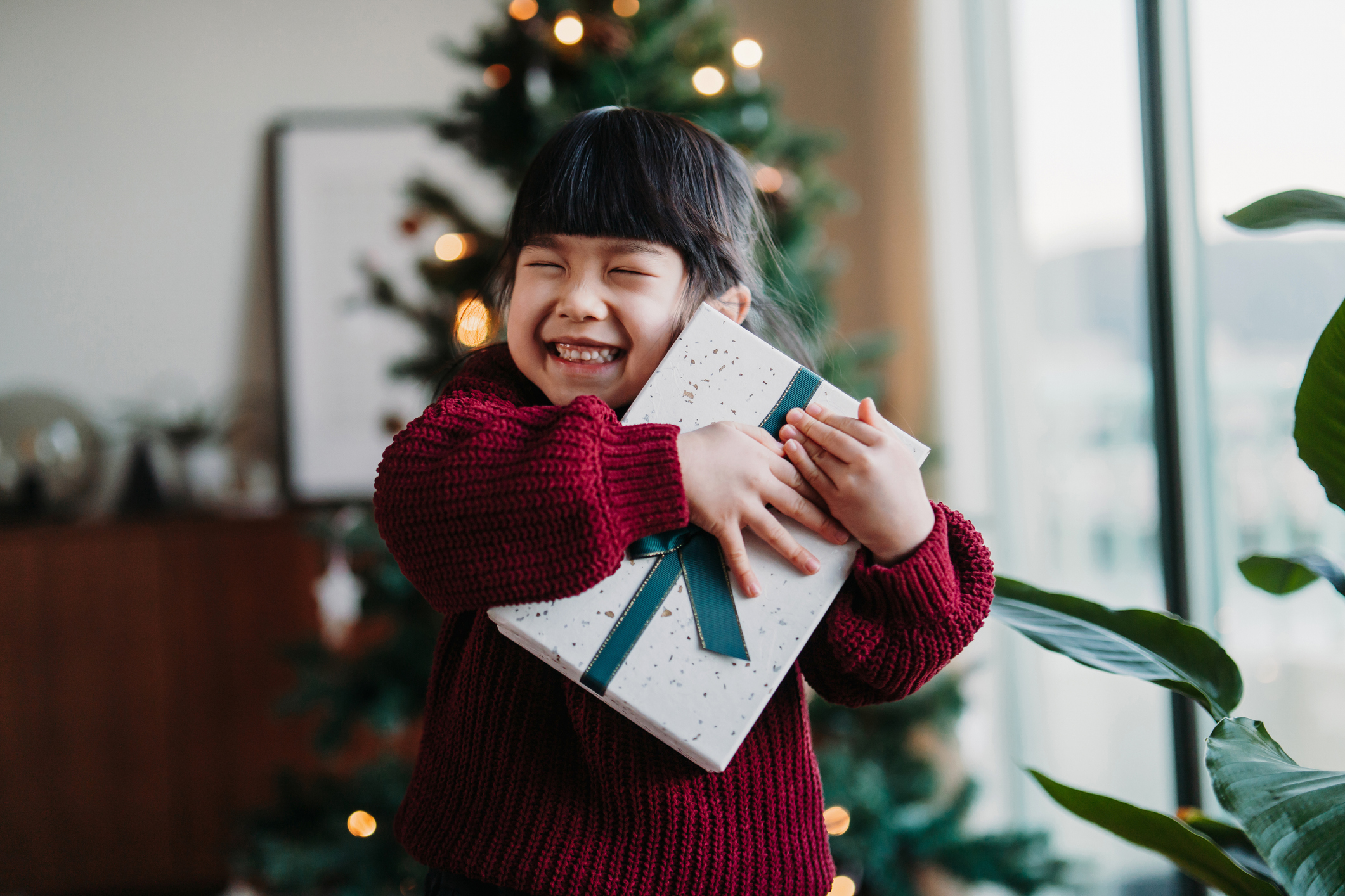 A little girl hugs a wrapped Christmas present with a big smile on her face.